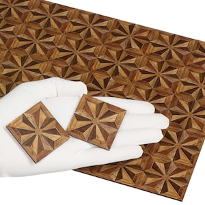 Puede incluir: Dos baldosas cuadradas de madera con un diseño de estrella se sostienen sobre una hoja más grande de suelo de madera. Las baldosas y el suelo presentan un patrón geométrico repetitivo en tonos marrones y beige.