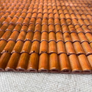 May include: A close-up of a brown tiled roof made of small, individual tiles. The tiles are arranged in a repeating pattern, creating a textured surface.