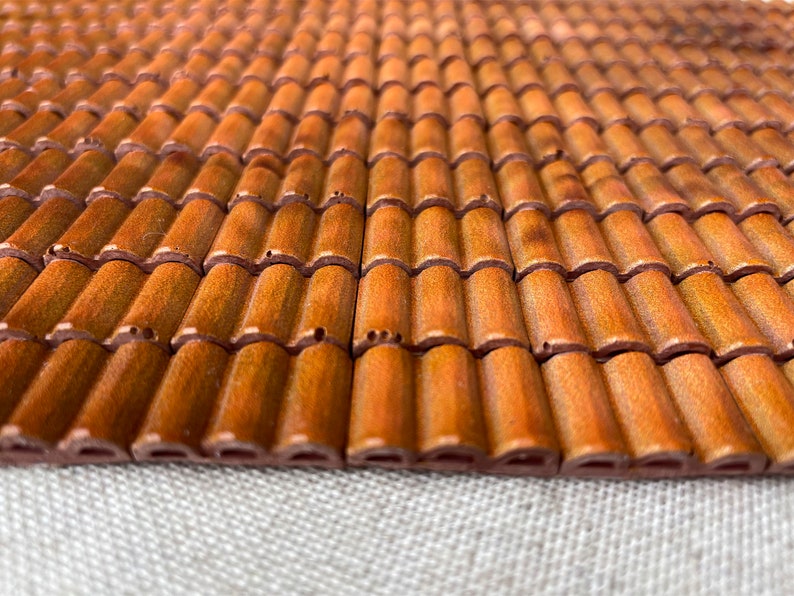 May include: A close-up of a brown tiled roof made of small, individual tiles. The tiles are arranged in a repeating pattern, creating a textured surface.