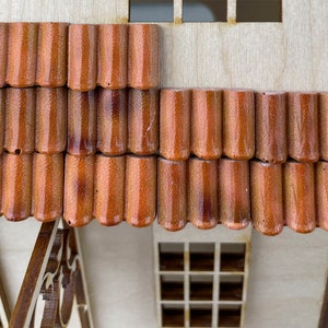 May include: Close-up of a wooden model house with brown tile roofing. The tiles are arranged in rows and have a slightly curved shape.
