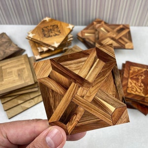 Könnte beinhalten: Ein Satz Holz-Untersetzer mit komplizierten geometrischen Mustern. Die Untersetzer sind aus verschiedenen Holzarten gefertigt und schaffen so ein einzigartiges und wunderschönes Design. Die Untersetzer sind perfekt, um jedem Zuhause einen Hauch von Eleganz zu verleihen.