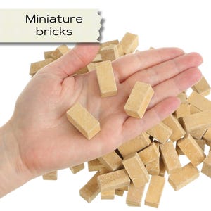 Op de afbeelding: Een hand die meerdere kleine, bruin-gele bakstenen vasthoudt. De bakstenen zijn rechthoekig en lijken van een lichtgekleurd materiaal te zijn gemaakt. De tekst "Miniature bricks" staat in een banner linksboven.