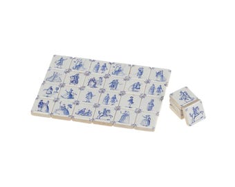Puede incluir: Un conjunto de baldosas de cerámica blancas con ilustraciones azules de figuras con vestimenta de época. Algunas baldosas están apiladas. Las baldosas están dispuestas en un patrón rectangular, con unas pocas baldosas apiladas al lado.
