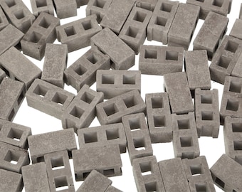 May include: A scattering of small, grey concrete blocks, each with two rectangular holes. The blocks are arranged on a white background. These blocks are likely for model building or decorative purposes.