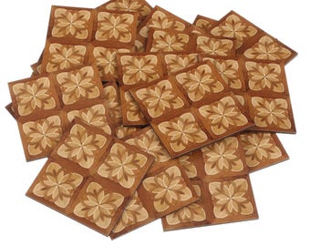 May include: A pile of square wooden tiles with a floral pattern. The tiles are a warm brown color with lighter beige and tan accents in the floral design. The tiles are arranged in a slightly overlapping manner.
