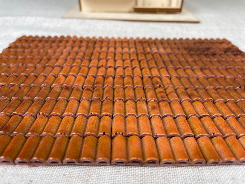 May include: A close-up of a miniature roof made of terracotta tiles. The tiles are arranged in a staggered pattern, creating a realistic look. The tiles are a warm brown color with a slightly textured surface.