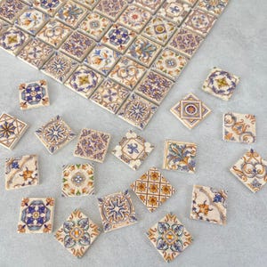 Peut inclure: Assortiment de carreaux de céramique décoratifs avec des motifs floraux et géométriques complexes dans des tons de bleu, jaune et blanc. Les carreaux sont disposés de manière dispersée sur une surface gris clair.