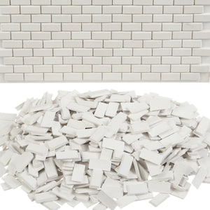 Op de afbeelding: Witte rechthoekige mozaïektegels in een baksteenpatroon, boven een stapel losse, gebroken tegels. De helderwitte tegels suggereren een strakke, moderne uitstraling. De afbeelding toont materialen voor doe-het-zelf- of knutselprojecten, met focus op tegels.