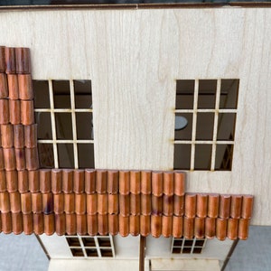 May include: A wooden model of a building with a brown tiled roof. The roof is made of individual tiles that are arranged in a pattern. The building has two windows on the top floor and one window on the bottom floor.