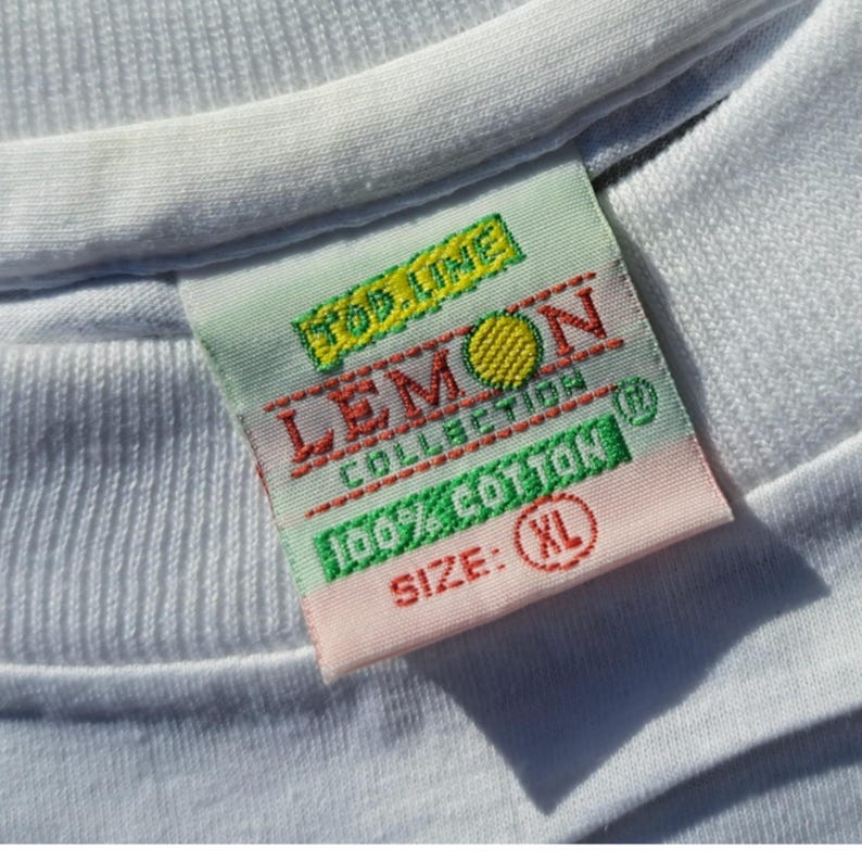 May include: White t-shirt tag with green, red, and yellow text that reads "Top Line Lemon Collection 100% Cotton" and "Size: XL".