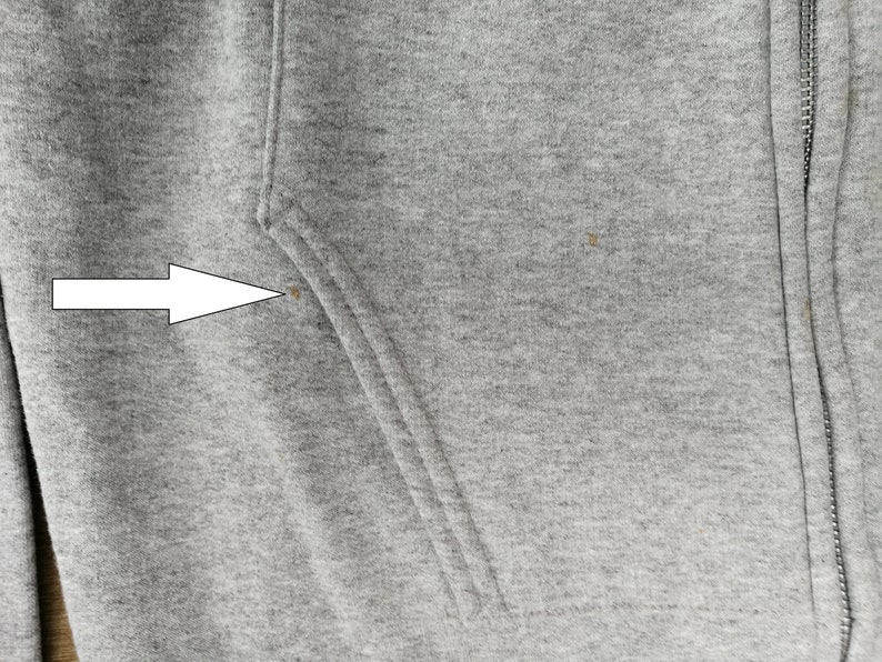 May include: Close-up of a gray hooded sweatshirt with a zipper. The sweatshirt has a small brown stain on the left side.