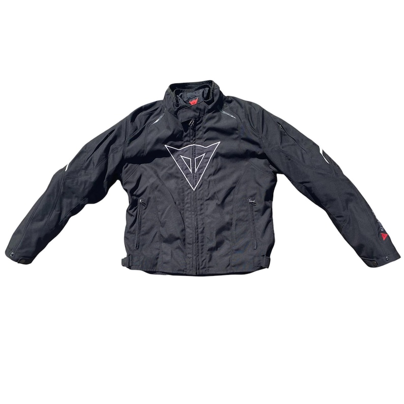 May include: Black motorcycle jacket with a white logo on the chest. The jacket has a high collar, zippered pockets, and white accents on the sleeves. Red accents are visible on the sleeves. The jacket is spread out on a white background.