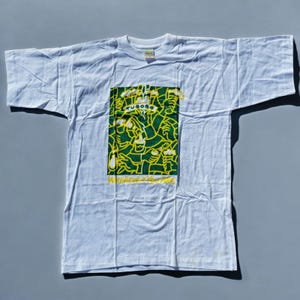May include: White t-shirt featuring a green and yellow graphic print of people holding up beer bottles. The graphic includes the text "Tuborg" and "Wherever you are".