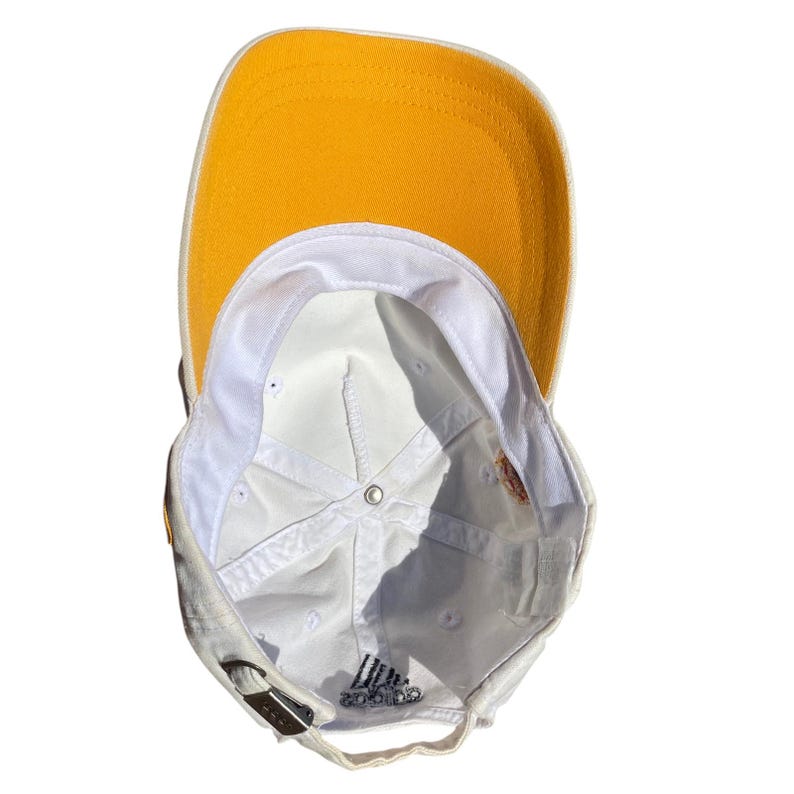 May include: A white baseball cap with a yellow brim. The underside of the cap is white, with the Adidas logo visible. The cap has a metal clasp for adjustment.