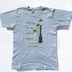 Peut inclure: Un t-shirt bleu clair avec un squelette de dessin animé portant un chapeau et tenant un livre. Le texte sur le t-shirt est "Waiting for the perfect woman" et "Jasper, Canada".