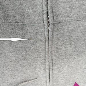 May include: Close-up of a gray hooded sweatshirt with a zipper. A small brown stain is visible on the fabric near the zipper.