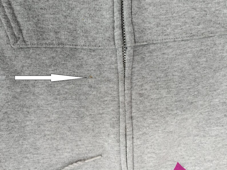 May include: Close-up of a gray hooded sweatshirt with a zipper. A small brown stain is visible on the fabric near the zipper.