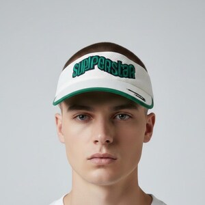 May include: White visor with green trim and the word "SUPERSTAR" in green lettering. The visor has a mesh texture and a curved brim. A stylish accessory for sports or casual wear.