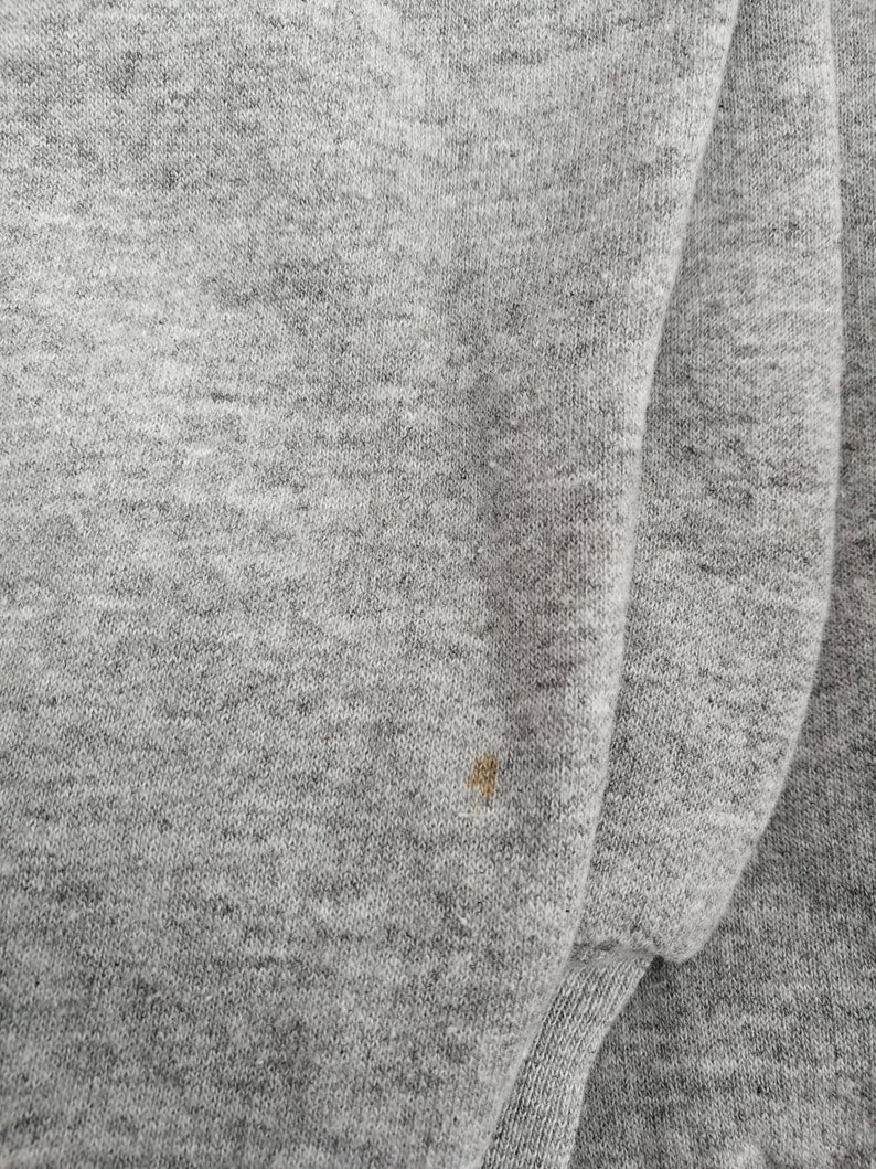 May include: A close-up of a gray sweatshirt with a small brown stain.