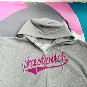 May include: Gray zip-up hoodie with a pink "fastpitch" graphic on the front.