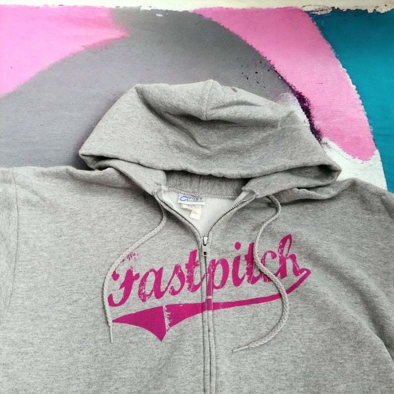 May include: Gray zip-up hoodie with a pink "fastpitch" graphic on the front.