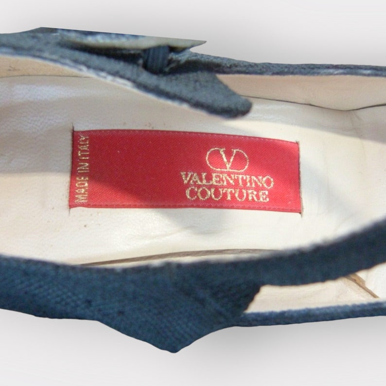 May include: Close-up of a navy blue shoe interior with a red label. The label reads "VALENTINO COUTURE" in gold lettering, with the "V" logo. The words "MADE IN ITALY" are also visible.