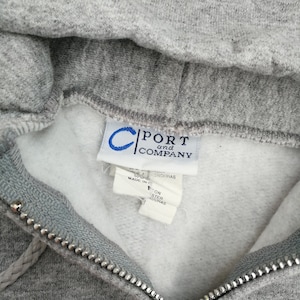 May include: Gray hooded sweatshirt with a zipper closure. The tag reads "Port and Company" and indicates the garment is made in Honduras.