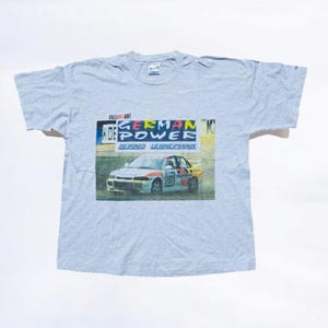 May include: A gray t-shirt with a graphic of a white rally car with the text "German Power" and "Bernd Leinemann" on it. The text "Rally Art" is also visible on the graphic.