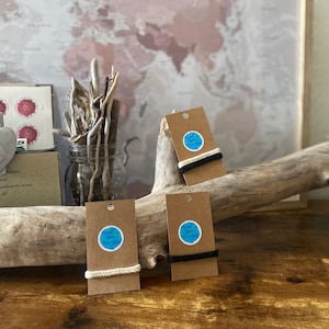May include: Three brown paper cards with white and black string attached. Each card has a blue circle sticker with the text "The Joy of Everyday" on it.