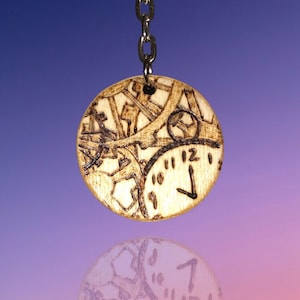 May include: A round, wooden pendant with a steampunk clock design. The pendant is attached to a silver chain. The design features clock hands pointing to 7 o'clock and gears. The pendant is made of light-colored wood with dark brown etched details.