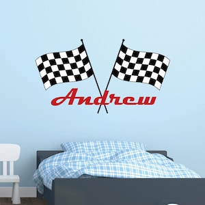 May include: Two crossed black and white chequered racing flags with the name "Andrew" in red script. The flags are on a light blue wall above a bed with a blue and white patterned duvet.