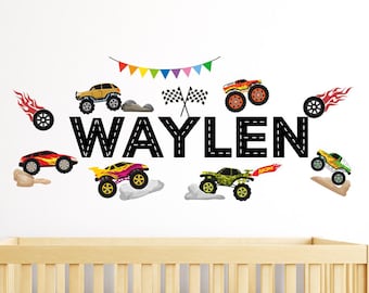 May include: A black and white wall decal with the name "WAYLEN" spelled out in a road design. The decal includes a string of colorful flags, checkered flags, and several cartoon monster trucks in various colors.