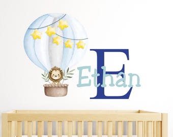 Peut inclure: Une décalcomanie murale de style aquarelle représentant une montgolfière bleu clair avec des étoiles jaunes et un lion. Le nom "Ethan" est affiché en lettres bleues et bleu clair, avec un grand "E" bleu.