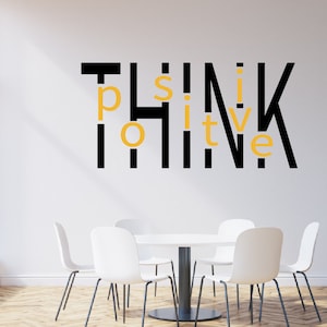 Pode incluir: Uma parede branca com letras pretas e amarelas que dizem "Think Positive". Há quatro cadeiras brancas e uma mesa branca em frente à parede.