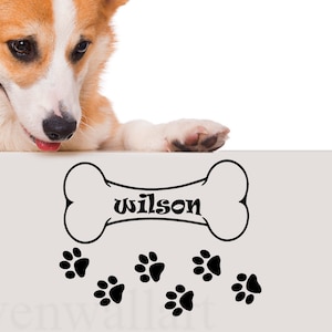May include: A white background with a black bone-shaped graphic with the word "wilson" inside. There are five black paw prints below the bone. A corgi dog is peeking over the top of the background.