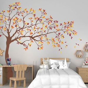 May include: A brown tree silhouette wall decal with orange, yellow, and red leaves. The decal is on a white wall in a bedroom with a bed, nightstand, and desk.