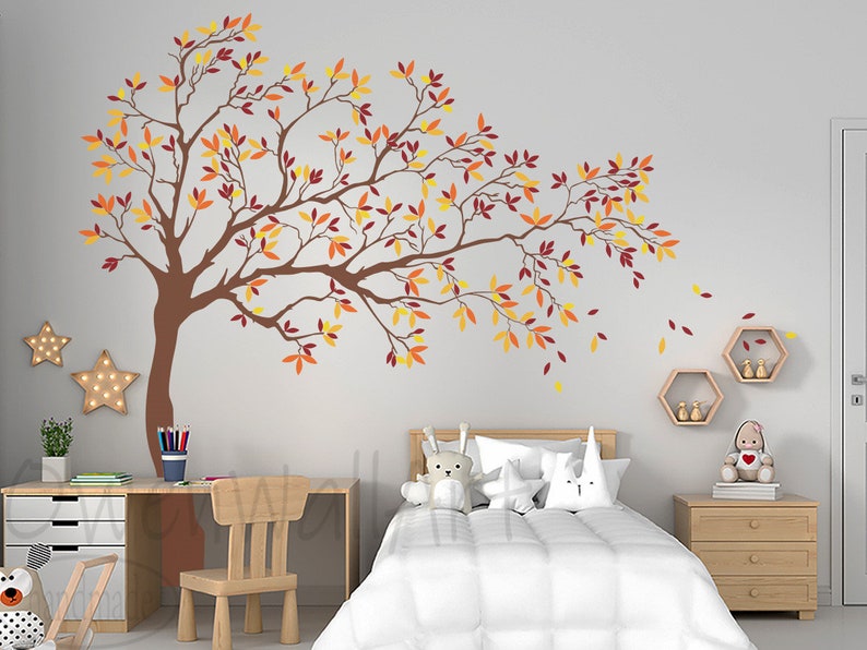 May include: A brown tree silhouette wall decal with orange, yellow, and red leaves. The decal is on a white wall in a bedroom with a bed, nightstand, and desk.