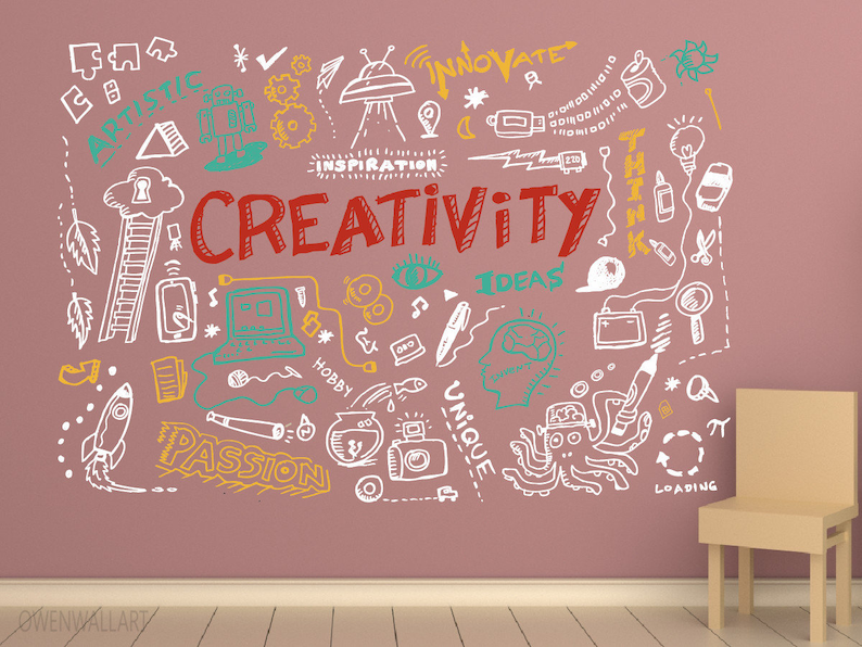 May include: A pink wall with white doodle art featuring the word "CREATIVITY" in red, surrounded by other words like "INSPIRATION", "IDEAS", "PASSION", "UNIQUE", and "HOBBY". There is a light brown chair in the lower right corner of the image.