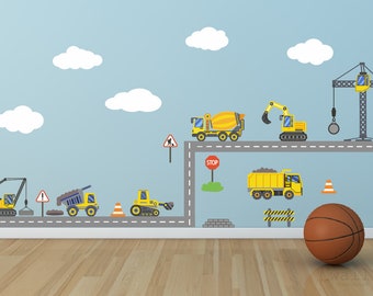 May include: A yellow construction vehicle wall decal set with a crane, dumper truck, cement mixer, excavator, and bulldozer. The decals are on a light blue wall with white clouds. There is a basketball on the floor.