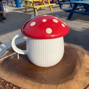 May include: White ceramic mug with a red and white polka dot mushroom lid. The mug is sitting on a wooden slice.
