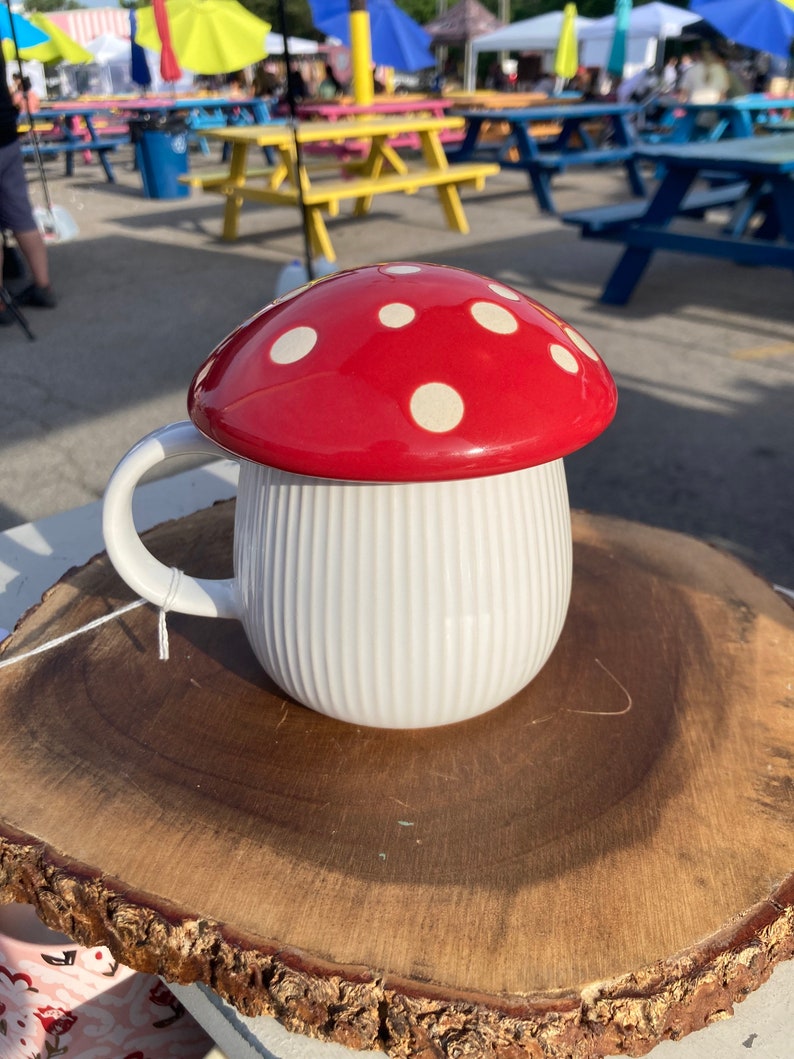 May include: White ceramic mug with a red and white polka dot mushroom lid. The mug is sitting on a wooden slice.