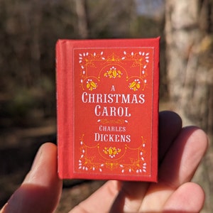 May include: A red book with a gold title that reads "A Christmas Carol" by Charles Dickens. The book has a decorative border with white and gold accents.