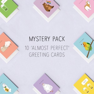May include: A set of 10 greeting cards with various illustrations. The cards are all white with colored backgrounds and feature cute cartoon animals and objects. The cards are arranged in a grid pattern on a light blue background. The text "MYSTERY PACK 10 'ALMOST PERFECT' GREETING CARDS" is displayed in the center of the image.