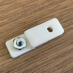 Puede incluir: Un soporte de pl&aacute;stico blanco con un agujero y un tornillo y una tuerca plateados.