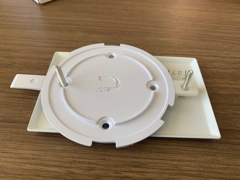 Puede incluir: Placa de pared blanca de pl&aacute;stico con dos tornillos y una tapa redonda blanca con un logotipo que dice "D" y un peque&ntilde;o dise&ntilde;o de puntos. La placa tiene la palabra "AAR" impresa.