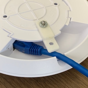 Puede incluir: Un router inal&aacute;mbrico blanco de techo con un cable Ethernet azul conectado a la parte posterior. El router tiene un bot&oacute;n de reinicio etiquetado como "Reset" y un peque&ntilde;o soporte de pl&aacute;stico blanco unido al lateral.
