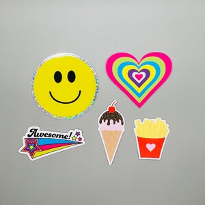 May include: A set of five colorful stickers featuring a smiley face, a heart with rainbow stripes, an ice cream cone, french fries, and a star with the word "Awesome!" on it.