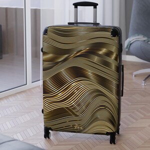 Puede incluir: Una maleta negra con ruedas con un diseño abstracto ondulado en dorado. La maleta tiene un asa telescópica y cuatro ruedas. El diseño es un patrón repetitivo de líneas curvas en tonos dorados y marrones.
