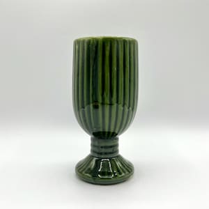 May include: A green ceramic goblet with a ribbed design. The goblet has a pedestal base and a rounded bowl. The color is a deep, forest green. The goblet is likely vintage or antique.