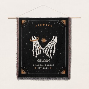 May include: Black woven tapestry featuring a design of two skeleton hands holding each other, with a ring on one finger. The text 'Till Death' is written below the hands, followed by 'Amanda + Robert Est. 2022'.